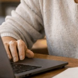 Pessoa sentada em sua casa, concentrada diante de um laptop sobre a mesa, em um ambiente acolhedor e bem iluminado