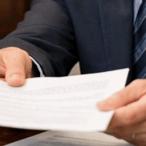 Imagem realista de um tabelião em seu escritório, olhando diretamente para quem vê a cena enquanto entrega um documento com expressão cordial e confiante