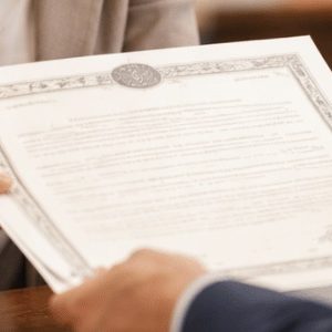 Pessoa recebendo uma certidão em balcão de cartório, em ambiente institucional moderno, com atendimento formal e iluminação natural suave, enquadramento em plano médio lateral e estilo fotográfico realista, sem textos ou símbolos visíveis.