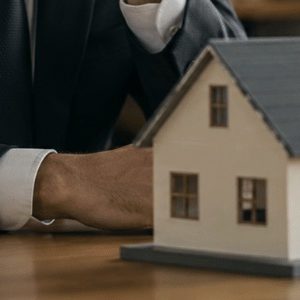 Homem analisando uma maquete de imóvel em ambiente jurídico, com elementos que remetem à justiça e processos de arresto de bens em um escritório sofisticado e realista.