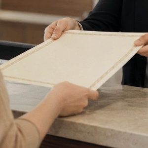 Funcionária de cartório entregando uma certidão a uma cliente em um balcão de atendimento, em ambiente institucional moderno e bem iluminado, transmitindo confiança, formalidade e agilidade no serviço.