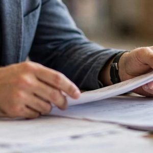 pessoa concentrada analisando documentos genéricos sobre mesa, com papéis espalhados
