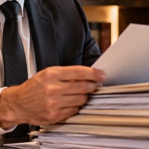 Advogado analisando atentamente uma pilha de documentos em seu escritório, em um ambiente profissional com iluminação suave e natural.